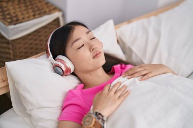 Çinli bir kadın yatak odasında müzik dinliyor.