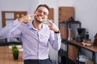 Ofisteki neşeli gülümseyen ve parmaklarıyla ve ağzıyla işaret eden genç İspanyol adam. diş sağlığı kavramı. 