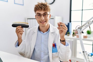 Young caucasian man wearing dentist uniform holding whitening and invisible aligner at clinic