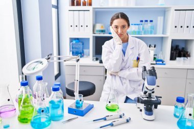 Young brunette woman working at scientist laboratory thinking looking tired and bored with depression problems with crossed arms. 