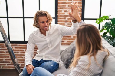 Man and woman couple high five with hands raised up sitting on sofa at new home