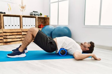 Genç İspanyol adam klinikte köpük silindiri kullanarak rehabilitasyon yapıyor.