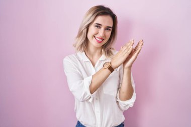 Pembe arka planda duran genç ve güzel bir kadın alkışlıyor ve alkışlıyor mutlu ve neşeli, gururlu elleri bir arada. 