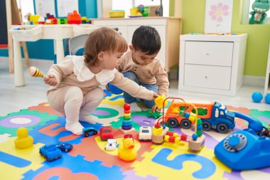Two kids playing with cars toy sitting on floor at kindergarten