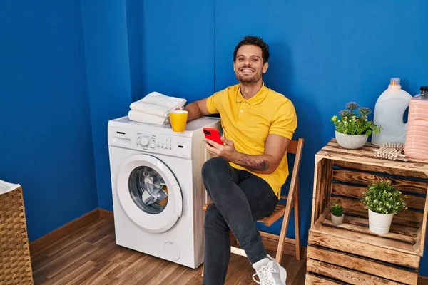 Ung Latinamerikan Man Dricka Kaffe Med Smartphone Wating För Tvättmaskin — Stockfoto