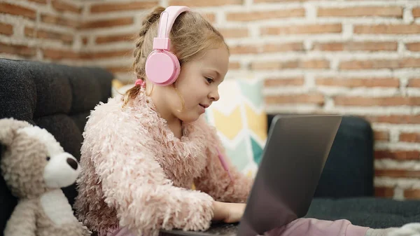 Adorable Blonde Girl Using Laptop Headphones Sitting Sofa Teddy Bear — Stok fotoğraf