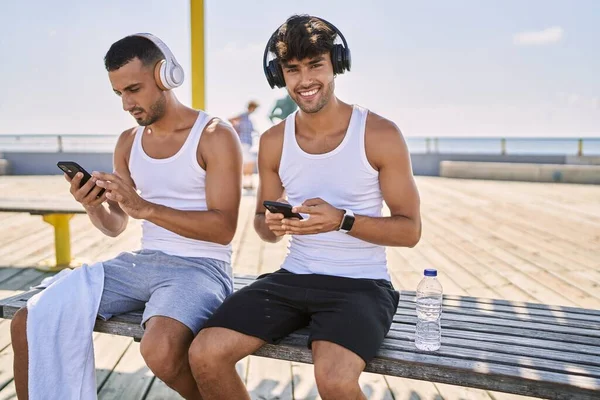 两只惊慌失措的男人用智能手机和耳机坐在海滨 — 图库照片