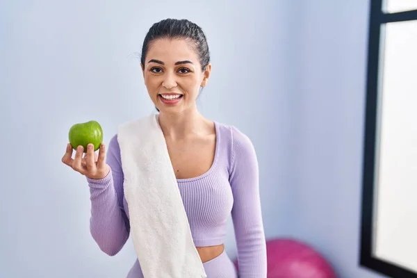 スポーツウェアとタオルを身に着けている若い女性は緑のリンゴを食べますポジティブで幸せな立って笑顔歯を示す自信を持って笑顔で笑顔 — ストック写真