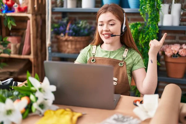 Redhead woman working at florist shop doing video call smiling happy pointing with hand and finger to the side