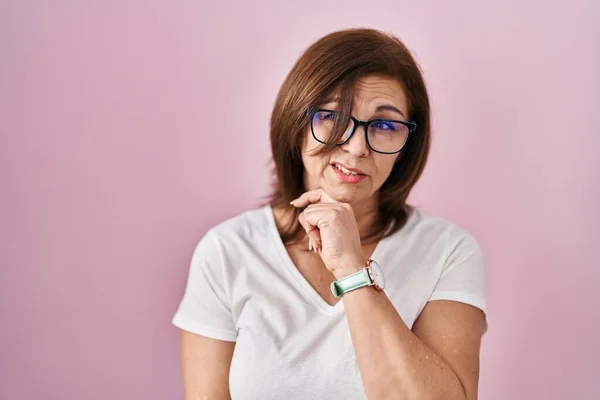 ピンクの背景の上に立っている中年のヒスパニック系の女性は 質問を心配し 心配し 顎に手で緊張 — ストック写真