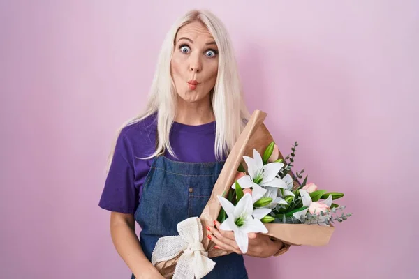 Caucasian woman holding bouquet of white flowers making fish face with lips, crazy and comical gesture. funny expression.