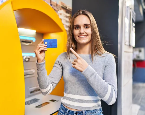 Young doctor woman holding credit card at cash point smiling happy pointing with hand and finger