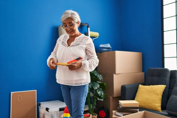 Middle age woman smiling confident choosing test paint color at new home