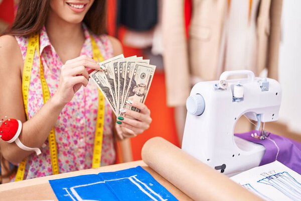 Young beautiful hispanic woman tailor smiling confident counting dollars at atelier