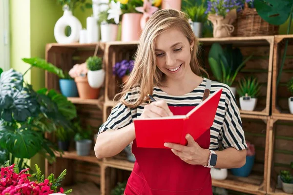 Joven Florista Mujer Rubia Sonriendo Escritura Segura Cuaderno Tienda Flores —  Fotos de Stock