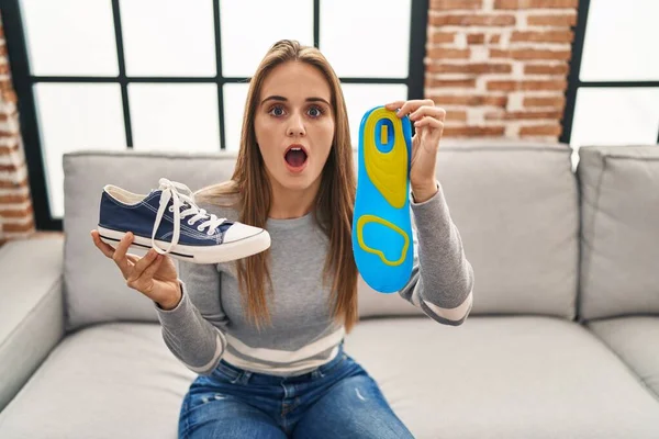Young woman holding shoe insole afraid and shocked with surprise and amazed expression, fear and excited face.