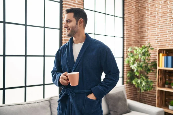 Young hispanic man wearing robe drinking coffee at home