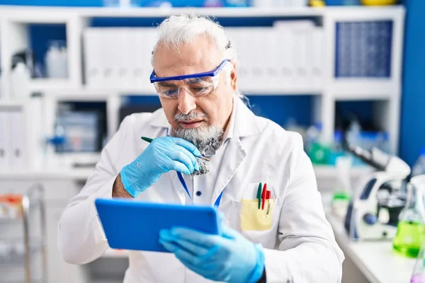 Middle age grey-haired man scientist using touchpad at laboratory