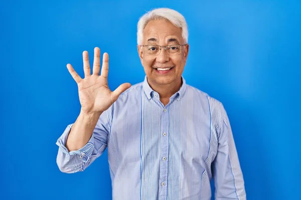 Hispanic senior man wearing glasses showing and pointing up with fingers number five while smiling confident and happy.