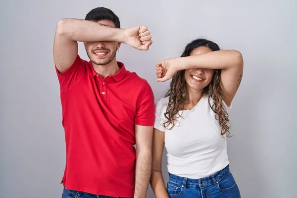 Young Hispanic Couple Standing Isolated Background Covering Eyes Arm Smiling — Stock Photo, Image