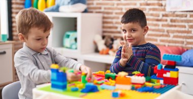 Two kids playing with construction blocks sitting on table at kindergarten