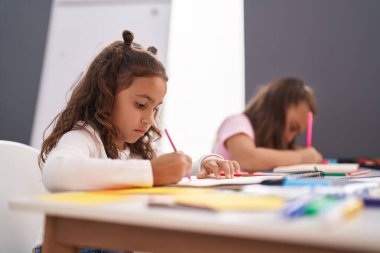 Two kids preschool students sitting on table drawing on paper at classroom