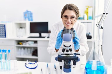 Laboratuvarda mikroskop kullanan genç İspanyol kadın bilim adamı üniforması giyiyor.