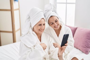 Mother and daughter wearing bathrobe having video call at bedroom