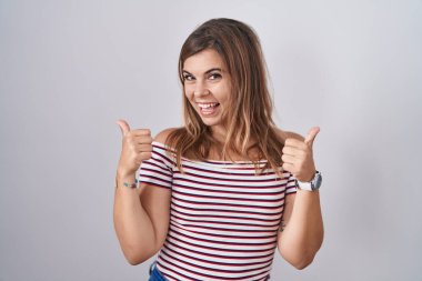 Arka planda izole edilmiş başarı işaretinin başında duran genç İspanyol kadın elleriyle olumlu jest yapıyor, gülümsüyor ve mutlu. Neşeli ifade ve kazanan jest. 