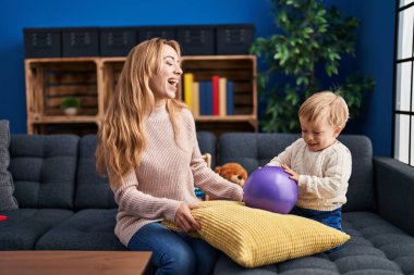 Mother and son playing with ball sitting on sofa at home