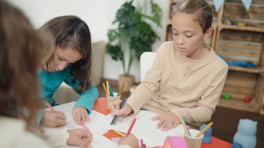 Two kids students sitting on table drawing on paper at kindergarten