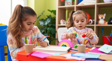 Two kids preschool students sitting on table drawing on paper at kindergarten