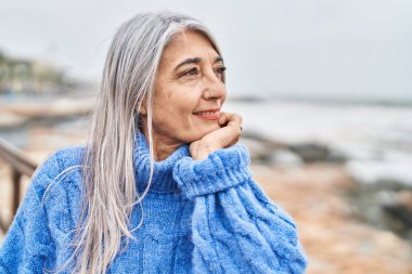 Middle age grey-haired woman smiling confident looking to the side at seaside