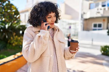 Genç, güzel İspanyol kadın akıllı telefonda konuşuyor parkta kahve içiyor.