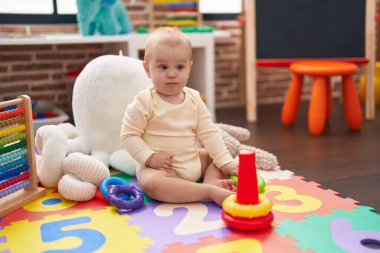 Anaokulunda yerde oturan sevimli beyaz bebek basketbol oyuncağıyla oynuyor.
