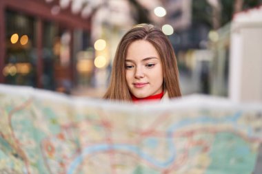 Young blonde woman smiling confident holding city map at street