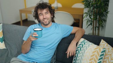 Genç İspanyol adam evdeki kanepede kahve içiyor.