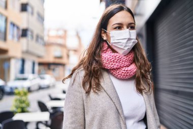 Young beautiful hispanic woman wearing medical mask and scarf at street