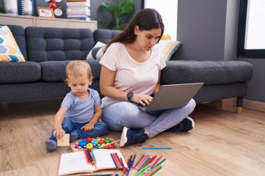 Anne ve oğlu dizüstü bilgisayar kullanıyor ve evde yerde oturuyor.