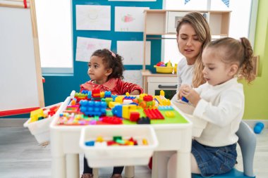 Teacher with girls playing with construction blocks sitting on table at kindergarten
