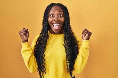 African woman standing over yellow background celebrating surprised and amazed for success with arms raised and open eyes. winner concept. 