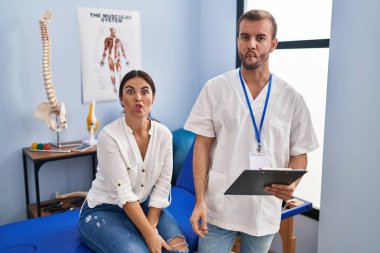 Young hispanic woman at physiotherapist appointment making fish face with lips, crazy and comical gesture. funny expression. 