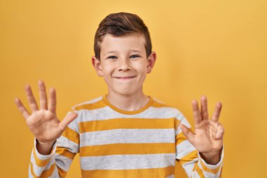 Young caucasian kid standing over yellow background showing and pointing up with fingers number nine while smiling confident and happy. 