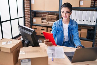 Young beautiful hispanic woman ecommerce business worker using touchpad and laptop at office