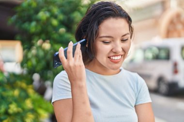 Young hispanic woman smiling confident listening audio message by the smartphone at street