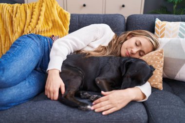Young blonde woman lying on sofa sleeping with dog at home