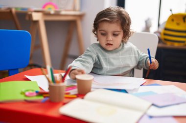 Anaokulunda masaya oturmuş kağıda resim çizen sevimli İspanyol kız öğrenci.
