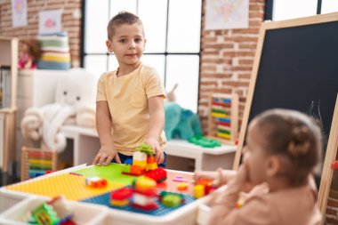 Anaokulunda inşaat bloklarıyla oynarken kendine güvenen iki çocuk.