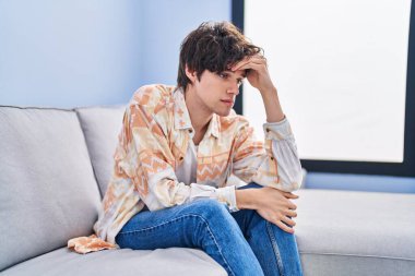 Young hispanic man stressed sitting on sofa at home
