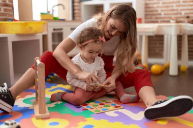 Teacher and toddler playing with maths puzzle game sitting on floor at kindergarten